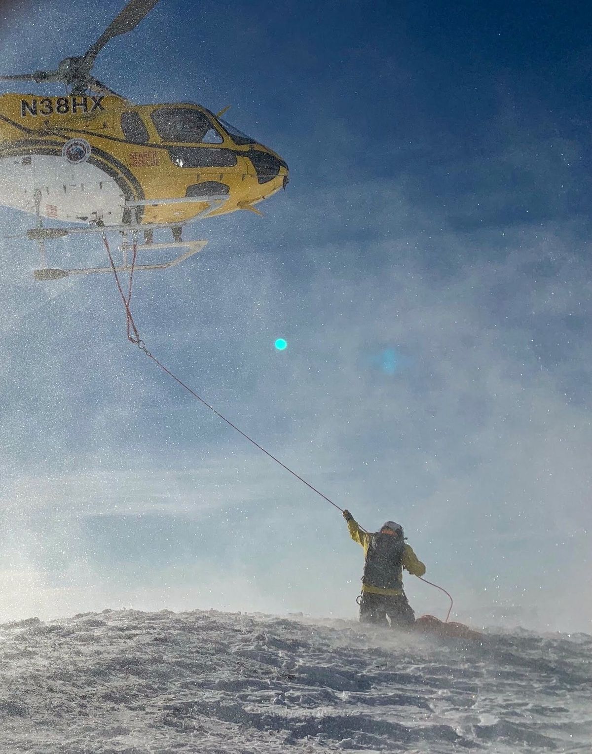 Teton County Search and Rescue helicopter hoisting a rescuer off a wind-blown ridge